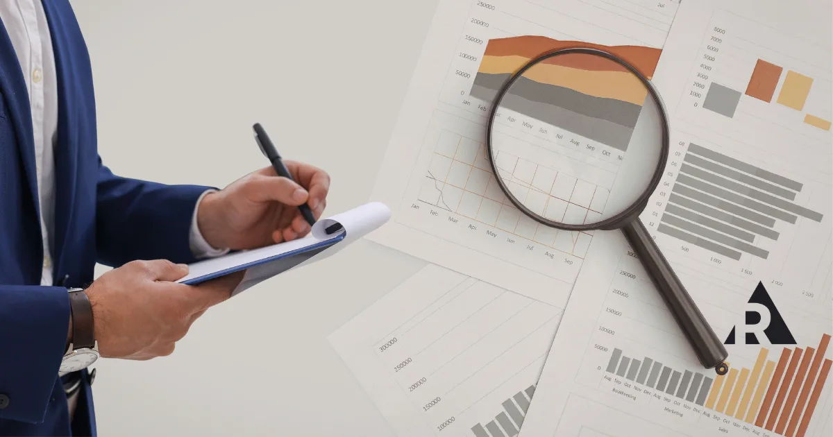 Person writing on a clipboard with a magnifying glass highlighting data on a business report, representing inspection and analysis.