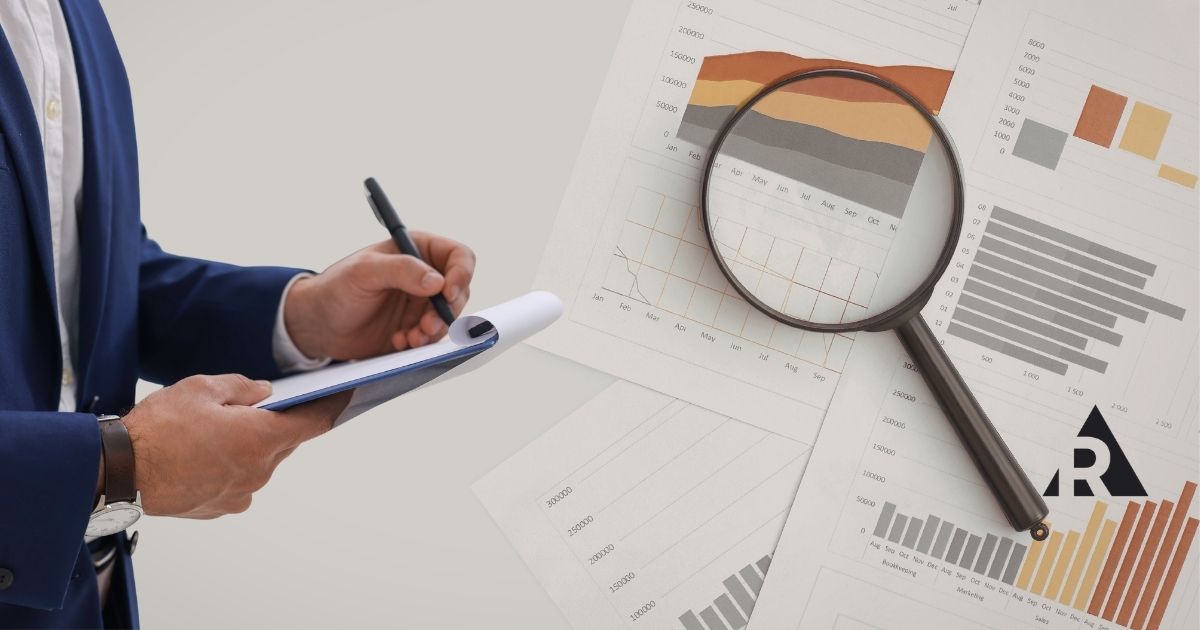 Person writing on a clipboard with a magnifying glass highlighting data on a business report, representing inspection and analysis.