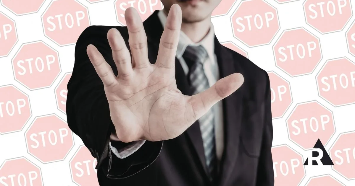 Person in a suit holding up a hand in a stop gesture against a background of stop signs