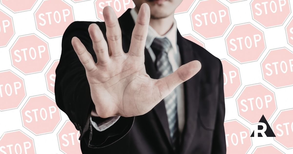 Person in a suit holding up a hand in a stop gesture against a background of stop signs