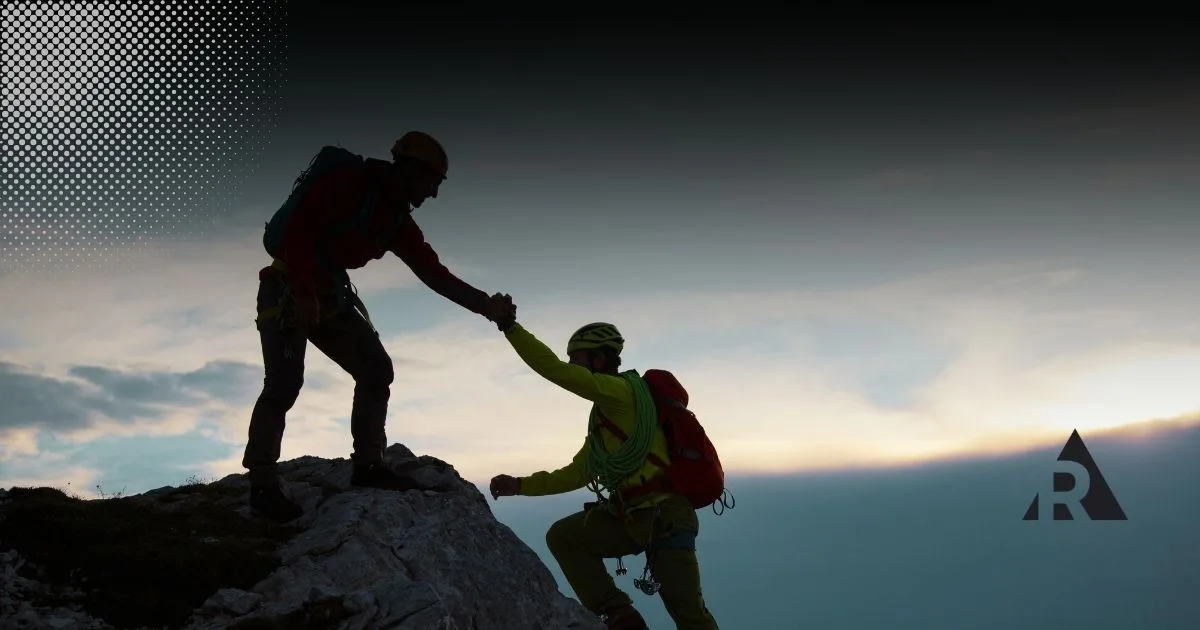 Man helping friend up a mountain